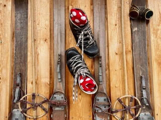 Close up of old leather hiking boots and wooden skis on facade of mountain hut. Alpine decor.
