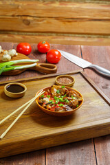 Thai chicken with rice and vegetables in a plate on a wooden table next to soy sauce sticks and vegetables in the background