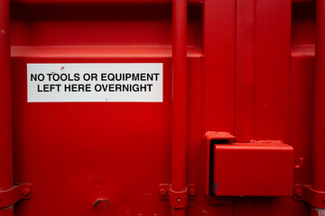 Red painted shipped container with a sticker warning of no tools left in the container. The...