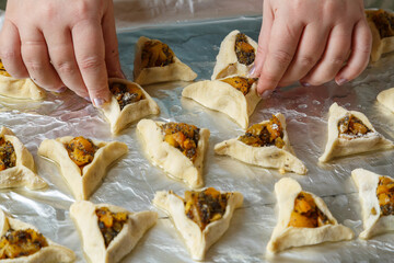 Women's hands put triangle gomentashi cookies on foil for baking, a treat for the holiday of Purim