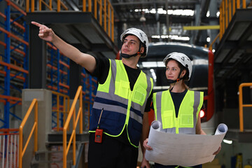 Male and female rail engineers working with blueprint drawing in electric train garage