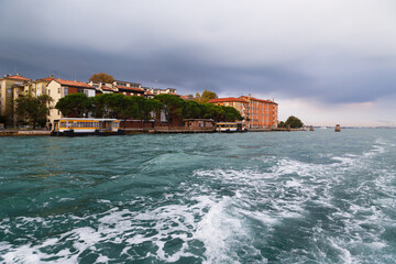 Venice vaporetto or water bus stop at Sacca Fisola island, Giudecca in Venetian Lagoon with dark blue stormy sky in background. Public transport route from cruise port in Venice, Italy. - obrazy, fototapety, plakaty
