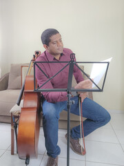 Music student playing cello and guitar at home, sitting, with music stand and sheet music.
