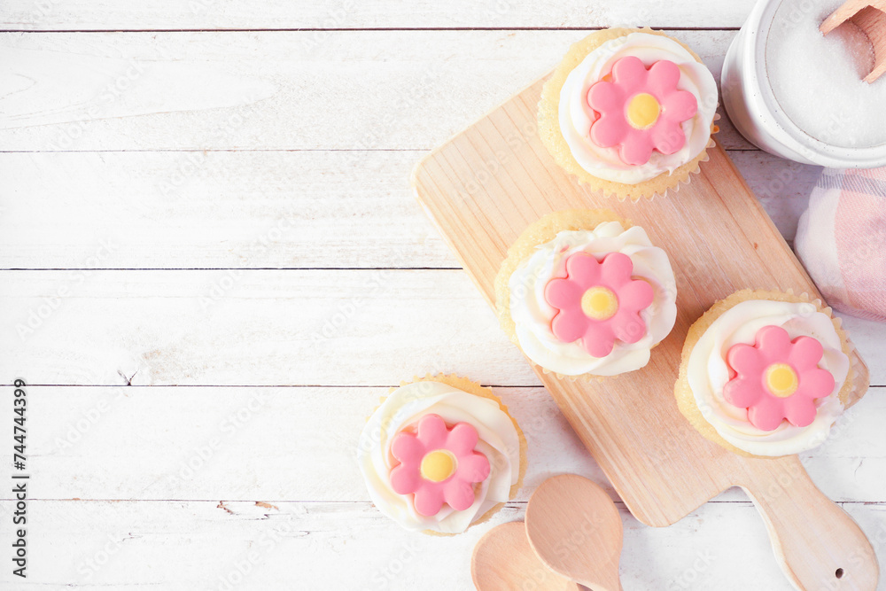 Poster pink spring flower cupcakes on a serving platter. top down view table scene with a white wood backgr
