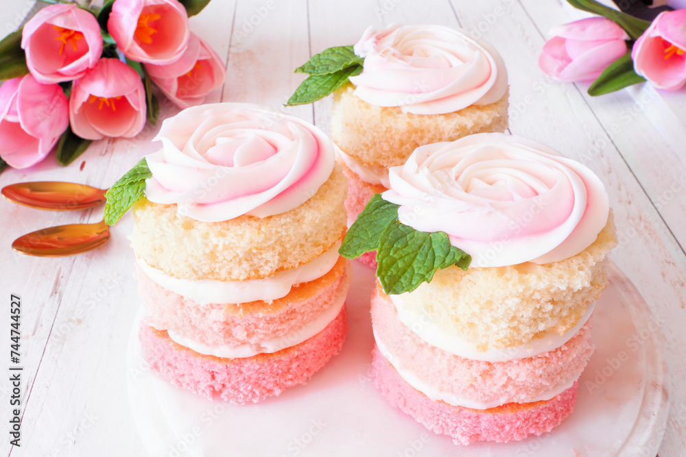 Poster spring mini cakes with buttercream rose. table scene with a white wood background. pink layers with 