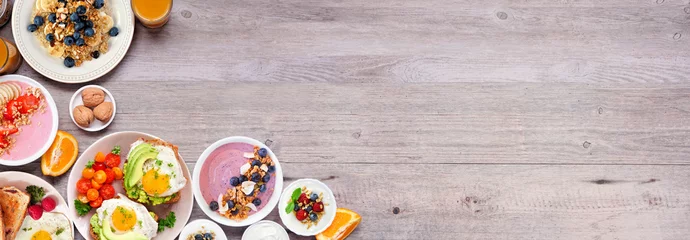 Fototapeten Healthy breakfast or brunch corner border on a wood banner background. Top down view. Avocado toast, smoothie bowls, oats, yogurt and assorted nutritious foods. © Jenifoto