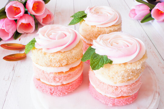 Spring mini cakes with buttercream rose. Table scene with a white wood background. Pink layers with flower topping.