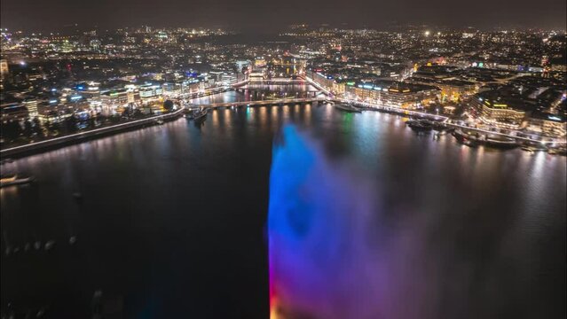Aerial hyper lapse shot of night city. Backwards fly above river surrounded by illuminated streets and buildings. Revealing Geneve lake with Jet d Eau water fountain. Geneva, Switzerland