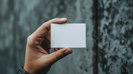 A person holding a white business card against a concrete wall backdrop
