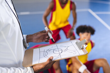 Coach outlines strategy on clipboard at indoor basketball court