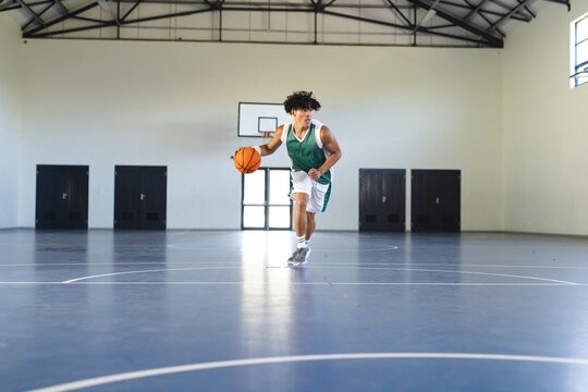 Young biracial man dribbles a basketball on an indoor court with copy space