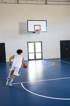 Young biracial man plays basketball indoors, with copy space