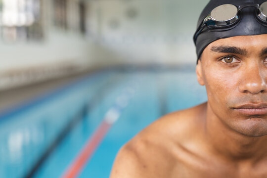 Focused young biracial male athlete swimmer at poolside, with copy space