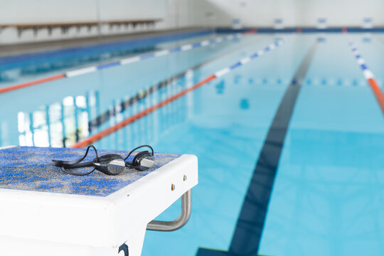 Swimming goggles rest on the edge of a pool in an indoor facility