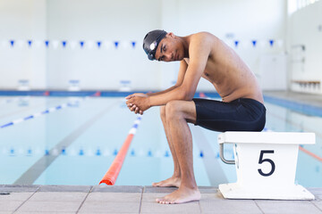 Young biracial male athlete swimmer sits thoughtfully by the poolside