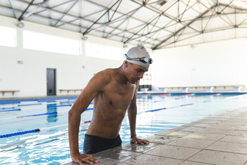 Young biracial male athlete swimmer rests at the poolside after swimming