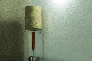 Mid-Century style table lamp with green shade against corner of two rough concrete walls