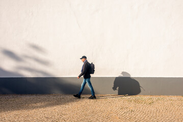 man with a backpack walking by a white wall, exercise.