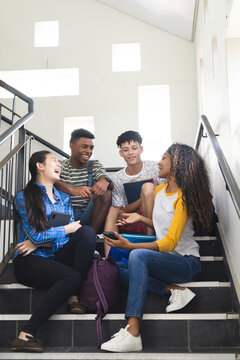 Teenage biracial boys and a teenage girl chat on high school stairs