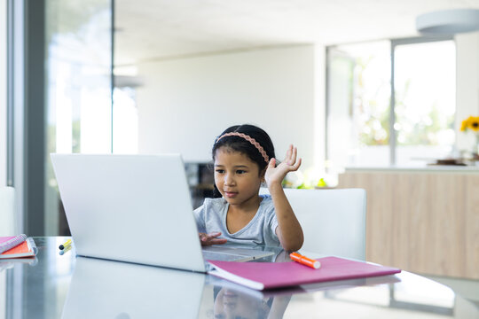 Biracial girl studies at a laptop in a bright home setting on a video call