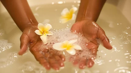Fototapeten preparing a bath with plumeria flowers for spa treatments. women's hands put flowers in the water © evastar
