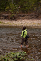 a woman in a green shirt is fishing in a river