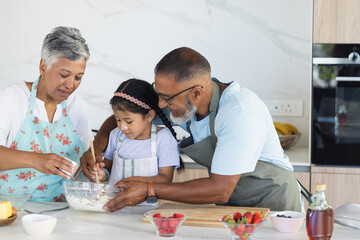Biracial grandparents and granddaughter enjoy baking together in a modern home kitchen