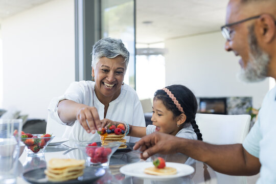 Biracial grandparents and granddaughter enjoy breakfast pancakes together at home
