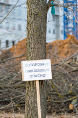 sign in Russian carefully cutting down trees dangerously near a tree against the backdrop of a construction site. concept of cutting down trees during construction