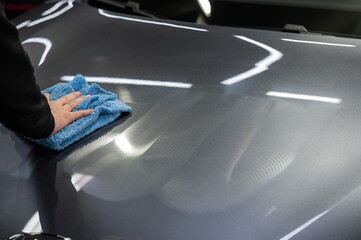 A man wipes the surface of the body of a gray car with a microfiber cloth. 