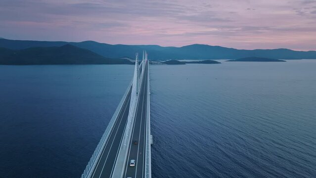 Aerial view of modern bridge crossing the Meditteranean sea in the evening. Beautiful sunset light and mountains in the background.