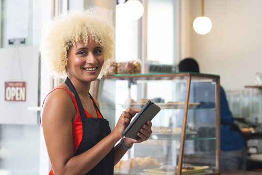A smiling biracial woman operates a point of sale system in a cafe, with copy space