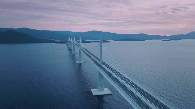 Majestic bridge across the blue sea at pink sunset. Mountains in the background. Aerial shot.
