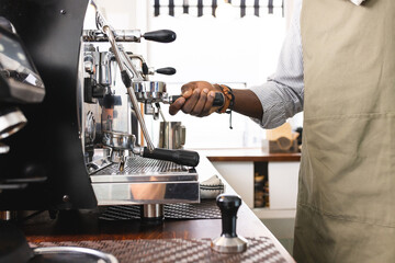 An African American barista operates an espresso machine at a cafe