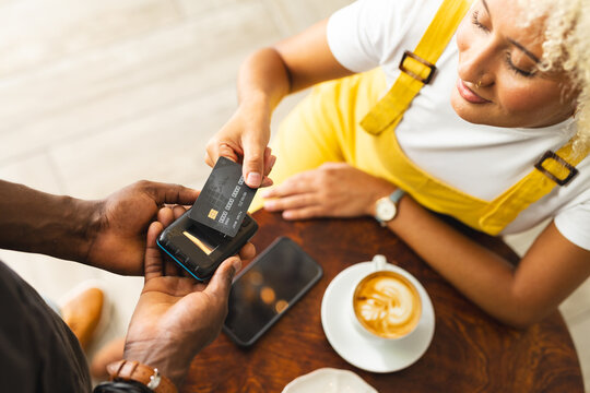Young African American man and biracial woman using a card for mobile payment at a cafe