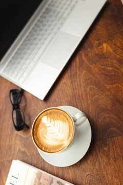 A cup of coffee sits on a wooden table next to a laptop and glasses with copy space