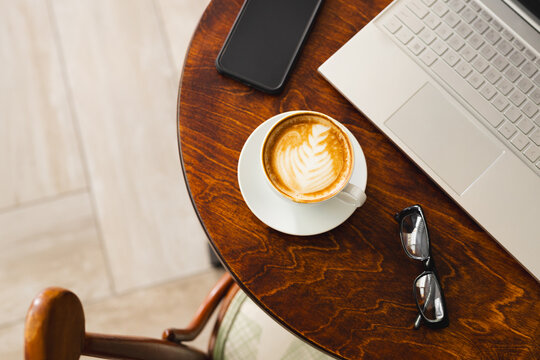 A laptop, coffee, and glasses rest on a wooden table with copy space