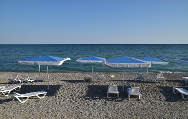 Sea beach with blue beach umbrellas and white sun loungers