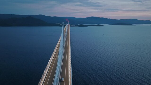 Majestic modern bridge across the calm sea in the evening. Sunset sky and mountains in the background. Aerial view. 