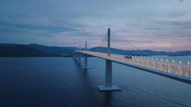 Majestic bridge with lights crossing the Mediterranean sea in the evening. Long bridge connecting land. Transportation concept.