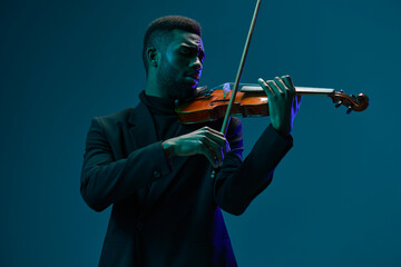 Elegant musician performing on violin in black suit against vibrant blue background