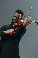 Elegant African American Man in Black Suit Performing on Violin Against Gray Background