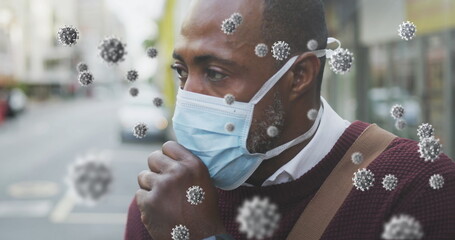 Covid-19 cells floating against african american senior man wearing face mask couching