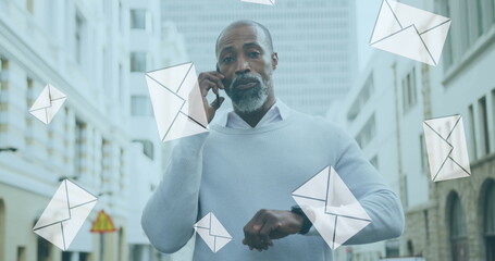 Image of digital mail envelope icons over african american man using smartphone in city