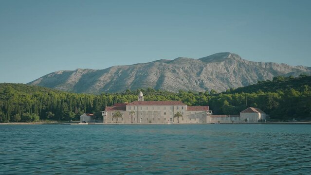 The view of Franciscan monastery from the blue sea on a sunny summer day. Visiting Badija island in Korcula. Beautiful mountains in the background. 