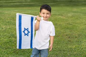 Smiling young boy proudly displaying the flag of Israel in a sunny park setting, expressing joy and patriotism.