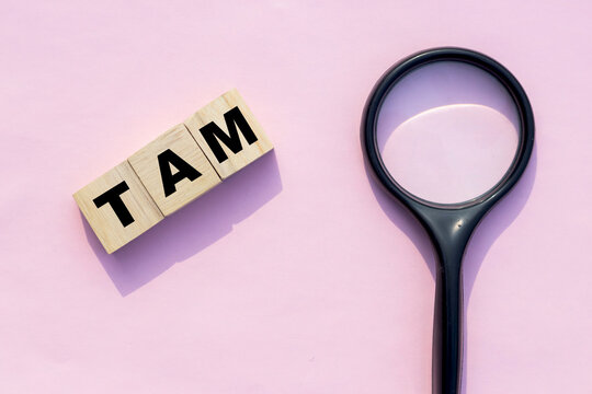 TAM word on wooden cube with magnifying glass Total Addressable Market business word concept