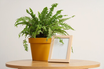 Blank frame with plant on table near light wall