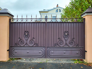There are brown iron gates with forged fragments between the light pillars