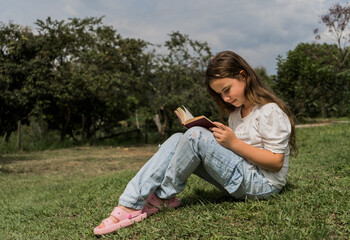 niña sentada al aire libre leyendo un libro  - obrazy, fototapety, plakaty